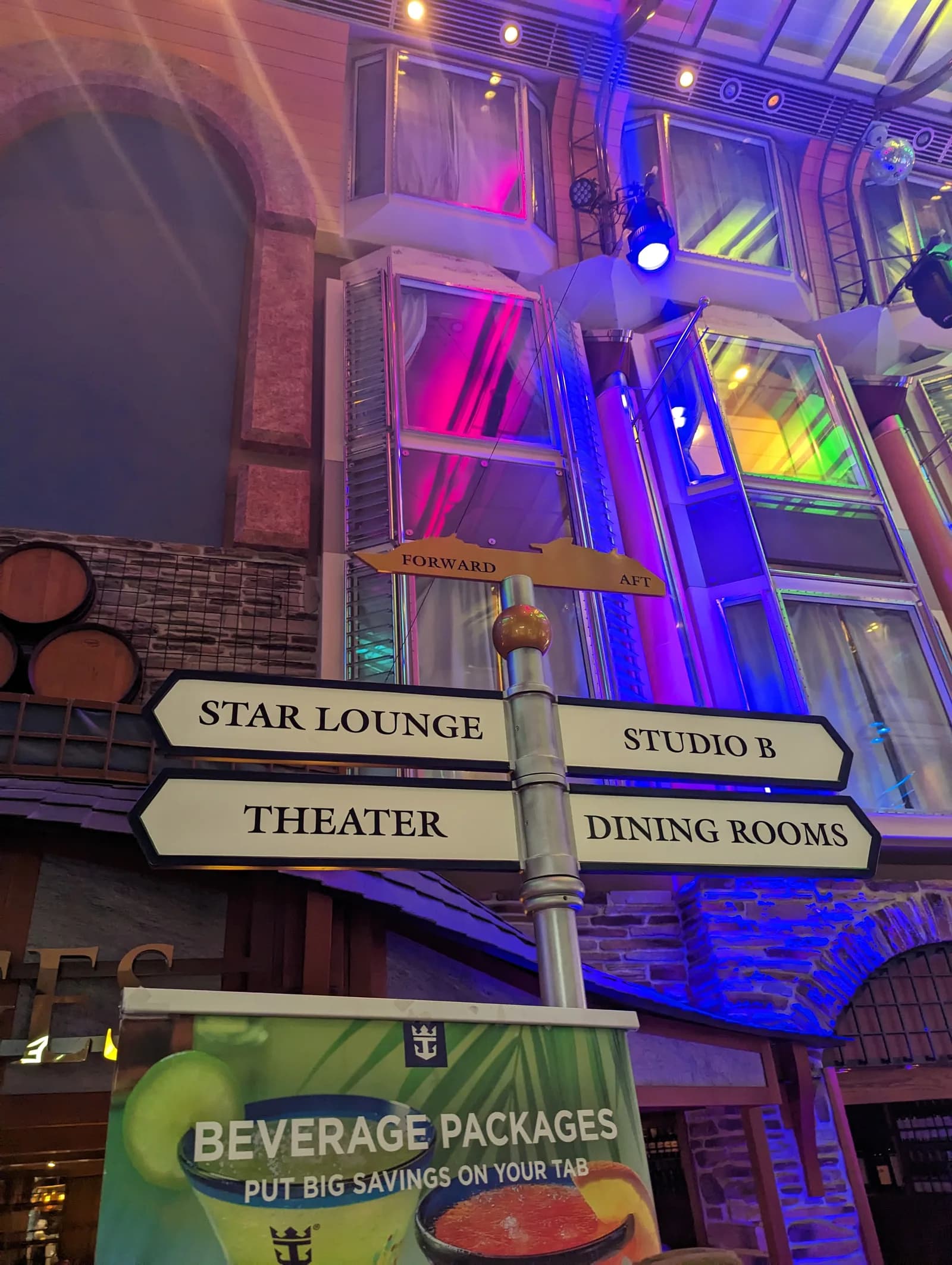 Signposts for the Star Lounge, Studio B, the theater and the dining rooms on the Royal Promenade of Royal Caribbean's Independence of the Seas, under colorful lit windows