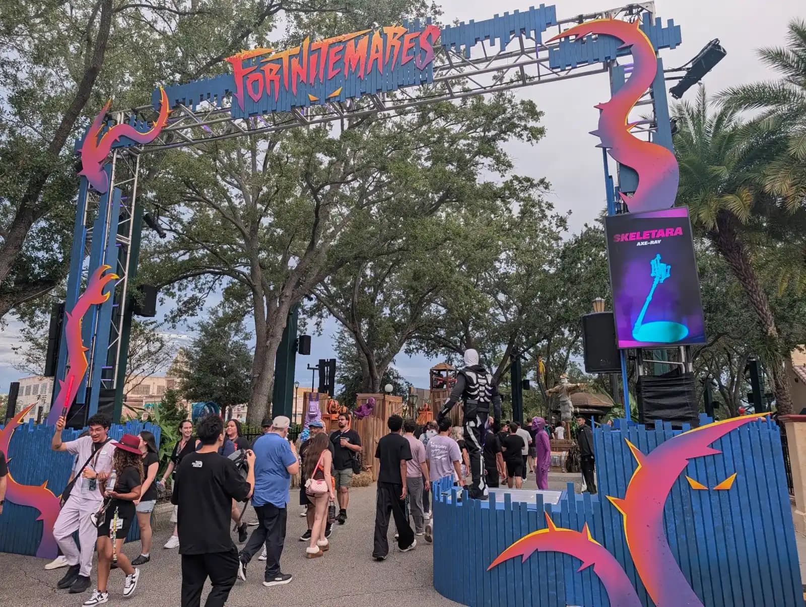 Guests walk under the FORTNITEMARES scare zone arch at Halloween Horror Nights 35, past a performer in a black skeleton suit and a screen showing the character Skeletara