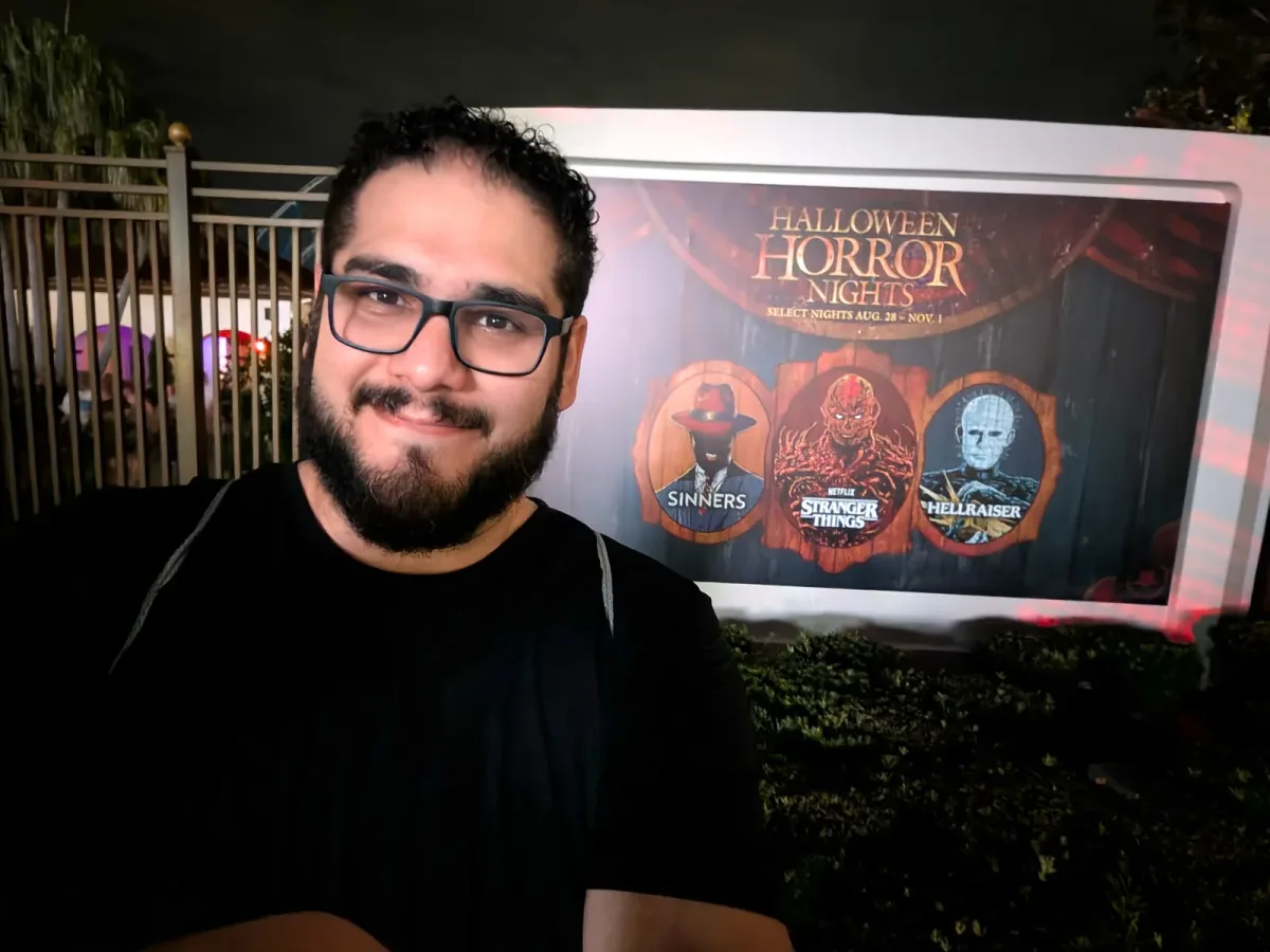 Pedro smiling in front of a Halloween Horror Nights sign that reads Select Nights Aug. 28 - Nov. 1, with artwork for the Sinners, Stranger Things and Hellraiser houses