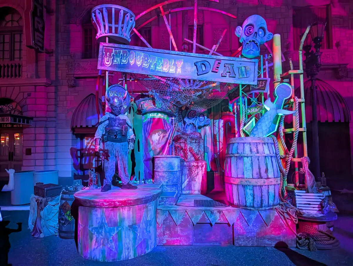 A scare zone set lit pink and purple, with an Undoubtedly Dead banner, a diver-suited figure, barrels and a giant fish