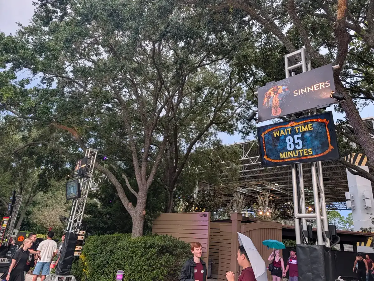 A Halloween Horror Nights wait-time board showing 85 minutes for the Sinners house, with guests walking past in early evening light